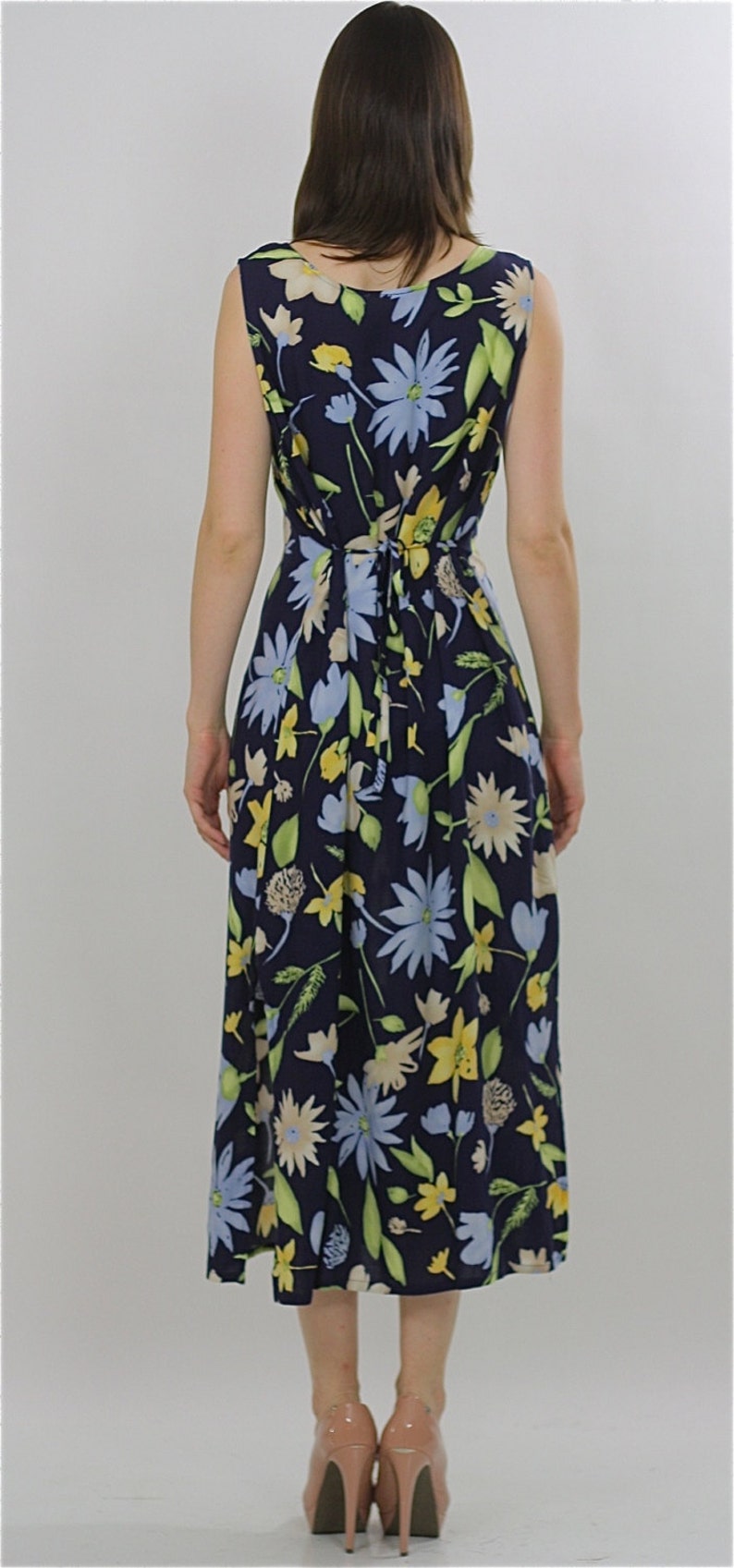 Pode incluir: Um vestido midi azul marinho com estampa floral com flores amarelas, azuis e verdes. O vestido tem um la&ccedil;o na cintura e &eacute; sem mangas.
