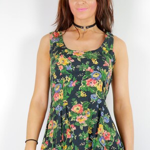 May include: A woman wearing a sleeveless, dark green dress with a floral print. The dress has a scoop neckline and a fitted bodice. The woman is wearing a black choker necklace with a silver pendant.