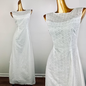 Könnte beinhalten: Ein weißes, ärmelloses Maxikleid mit einem zarten Lochmuster. Das Kleid hat einen runden Ausschnitt und einen taillierten Oberteil.