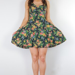 May include: A woman wearing a black floral print dress with a fitted bodice and a flared skirt. She is wearing black heeled sandals.