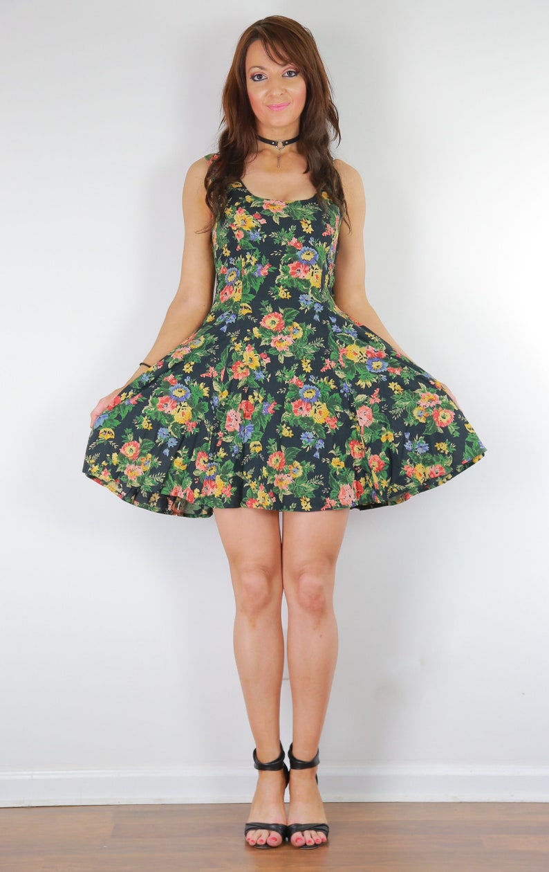 May include: A woman wearing a black floral print dress with a fitted bodice and a flared skirt. She is wearing black heeled sandals.
