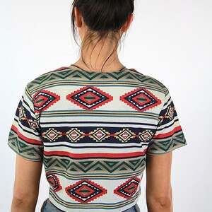 May include: A cropped, short-sleeved shirt with a colorful geometric pattern in shades of red, blue, green, and white. The shirt has a relaxed fit and a rounded neckline.