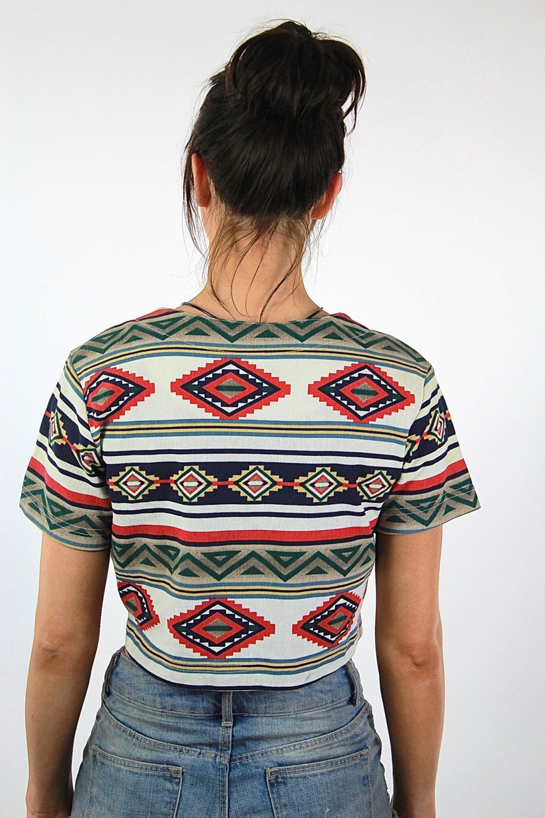 May include: A cropped, short-sleeved shirt with a colorful geometric pattern in shades of red, blue, green, and white. The shirt has a relaxed fit and a rounded neckline.