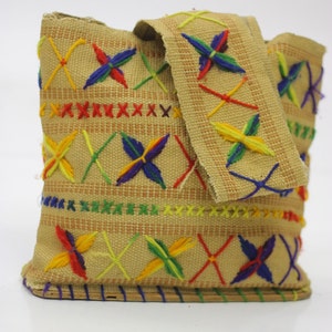 Peut inclure: Un petit sac en toile beige avec un motif brodé coloré. La broderie présente un motif répétitif d'étoiles multicolores et de X.