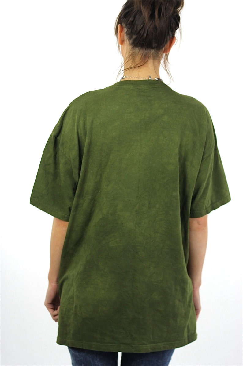 May include: A green t-shirt with a faded, tie-dye pattern. The shirt has a crew neck and short sleeves.