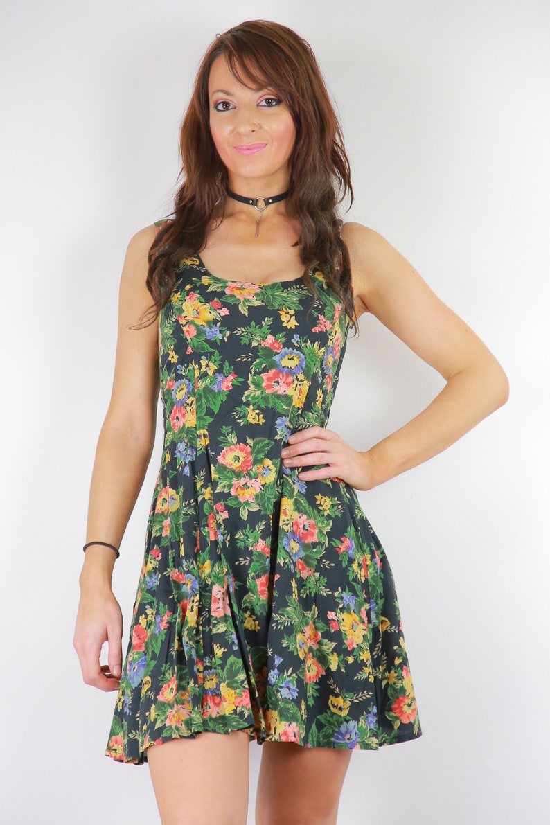 May include: A sleeveless, dark green dress with a floral print featuring pink, yellow, and blue flowers. The dress has a scoop neck and a fitted bodice.