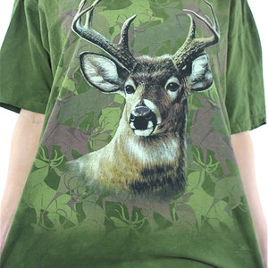 May include: Green t-shirt with a large print of a white-tailed deer with antlers in a camouflage pattern.