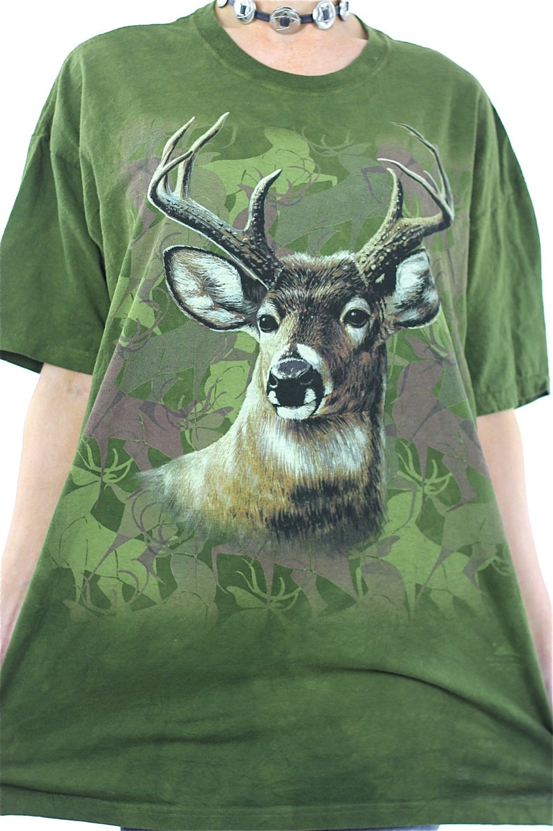 May include: Green t-shirt with a large print of a white-tailed deer with antlers in a camouflage pattern.