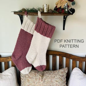 May include: Two hand-knitted Christmas stockings hanging from a wooden shelf. One stocking is maroon with a cream cuff and toe, while the other is cream with a maroon cuff and toe. The text PDF KNITTING PATTERN is visible on the right side.