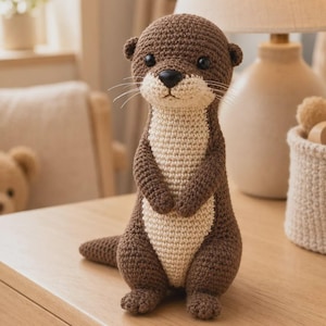 Könnte beinhalten: Ein gehäkeltes Otter-Stofftier in Braun und Creme. Der Otter hat einen dunkelbraunen Kopf, Rücken und Schwanz sowie eine hellere cremefarbene Brust und Schnauze. Er besitzt kleine schwarze Perlenaugen, eine schwarze Nase und feine weiße Schnurrhaare.