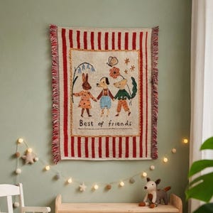 May include: A woven wall tapestry featuring a cream-coloured centre with an illustration of a rabbit, a dog, and a mouse holding hands, with the text Best of friends. The tapestry has red and white vertical stripes and a fringed edge on the sides.
