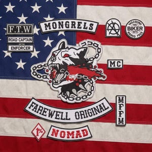 Op de afbeelding: Een verzameling geborduurde patches met een centrale grommende hondenkop met kettingen, omringd door tekstpatches waaronder MONGRELS, FAREWELL ORIGINAL, NOMAD, F.T.W, ROAD CAPTAIN, ENFORCER, MC, MFPM en een 1% ruitvormige patch op een vlagachtergrond.