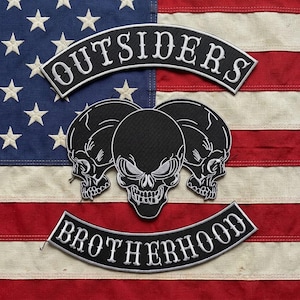 May include: A set of three embroidered patches featuring a black arched top rocker with the white text OUTSIDERS, a central emblem of three stylized black and white skulls, and a black arched bottom rocker with the white text BROTHERHOOD.