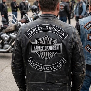 Op de afbeelding: Een zwart leren jack met een verweerde uitstraling en een grote geborduurde Harley-Davidson-patch op de rug. De patch bevat de tekst Harley-Davidson, Motor Harley-Davidson Cycles en Motorcycles in witte letters op een zwarte achtergrond.