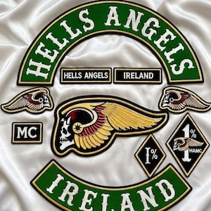 May include: A collection of embroidered patches including a large green arch with HELLS ANGELS text, a green IRELAND arch, a central winged skull emblem, two smaller winged skull patches, a rectangular MC patch, and two diamond-shaped 1% patches.