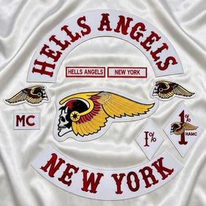 Könnte beinhalten: Eine Sammlung bestickter Aufnäher mit dem Text HELLS ANGELS und NEW YORK in Rot auf weißem Stoff. Enthält ein großes geflügeltes Totenkopf-Emblem, zwei kleinere geflügelte Totenkopf-Aufnäher, zwei rautenförmige 1%-Aufnäher und einen kleinen MC-Aufnäher.