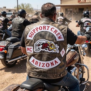 May include: A distressed brown leather motorcycle vest featuring a large back patch with the text SUPPORT CREW, MC, and ARIZONA in red, along with a graphic of a flaming skull and a diamond-shaped patch with the symbol 1% on the right side.