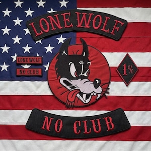 Könnte beinhalten: Ein Set aus gestickten Aufnähern auf einer Flagge der Vereinigten Staaten. Die Aufnäher umfassen einen großen runden Wolfskopf, zwei geschwungene Schriftzüge LONE WOLF und NO CLUB, zwei kleine Rechtecke und einen rautenförmigen 1%-Aufnäher in Rot und Schwarz.