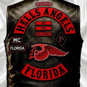 May include: A black leather vest featuring red embroidered patches. The back displays the text HELLS ANGELS, NOMADS, FLORIDA, MC, 666, AFFA, and 1% inside a diamond shape. A red winged skull emblem is centered above a large curved FLORIDA patch.