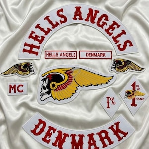 Op de afbeelding: Een verzameling geborduurde patches met de tekst HELLS ANGELS en DENMARK in rood op witte stof. Bevat een groot embleem met een gevleugelde schedel, twee kleinere patches met gevleugelde schedels, een MC-patch en twee ruitvormige 1%-patches.