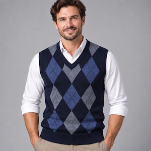 Puede incluir: Un chaleco de punto azul marino con cuello en V y un patrón de rombos repetitivo en tonos azul claro y gris. El chaleco se lleva sobre una camisa blanca de manga larga con botones, con las mangas remangadas hasta los codos.