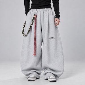 May include: Light gray wide-leg sweatpants featuring an elastic waistband, side pockets, and a black embroidered logo reading RVNTENG. A braided decorative cord in green, white, and red hangs from a metal clip attached to the front belt loop.