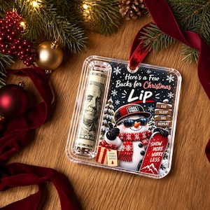 Può includere: Un portadenaro rettangolare in acrilico trasparente contenente una banconota da cento dollari arrotolata. Il design mostra un pupazzo di neve con occhiali da sole e cappello rosso, con il testo Here's a Few Bucks for Christmas Lip, Eat Sleep Ski Repeat e Snow More Worry Less.