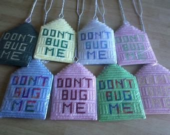 Könnte beinhalten: Acht gehäkelte, hausförmige Ornamente mit dem Text "Don't Bug Me" in verschiedenen Farben, darunter Grün, Gelb, Blau, Rosa und Weiß.