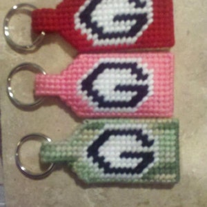 May include: Three keychains with a white letter G on a red, pink, and green background. Each keychain has a silver key ring.