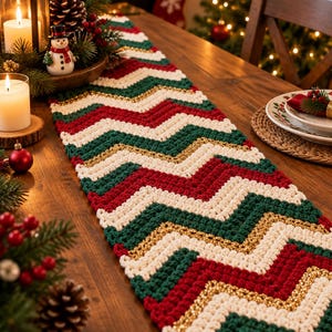 May include: A rectangular crochet table runner featuring a repeating chevron pattern in alternating stripes of dark green, bright red, cream, and metallic gold yarn. The textile has a textured, thick stitch construction and lies flat on a wooden surface.