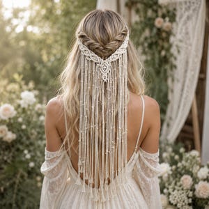 May include: A cream-coloured macrame hair accessory featuring an intricate braided headband design with long, dangling knotted fringe strands that cascade down the back, crafted from woven cotton cord with a central decorative knot pattern.