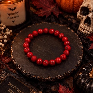 Peut inclure: Un bracelet élastique circulaire composé de perles rondes et lisses d'un rouge éclatant, présentant de subtiles veines sombres. Les perles sont de taille uniforme et enfilées sur un cordon élastique, formant une boucle continue de sphères en pierre polie.