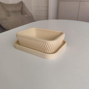 May include: A rectangular cream-colored planter with a matching drip tray. The planter features a textured exterior with diagonal, slanted grooves running along all four sides, creating a consistent pattern around the entire vessel.