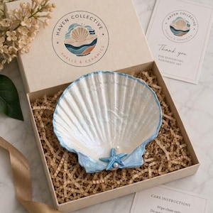 May include: A white and light blue scalloped shell dish featuring a small blue starfish and a white pearl accent, nestled in a cardboard gift box with shredded paper filler, a branded Haven Collective logo, and printed care instruction cards.