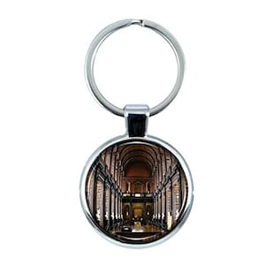 May include: Silver key chain with a round, silver-rimmed photo charm featuring a black and white photo of a long, arched hallway with bookshelves on either side.