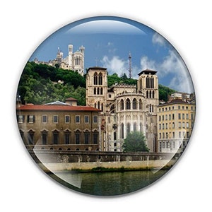 Puede incluir: Una postal con una vista panorámica de la basílica de Notre-Dame de Fourvière en Lyon, Francia. La basílica es un hito destacado con una fachada blanca y una alta aguja. La postal también muestra un río y edificios circundantes.