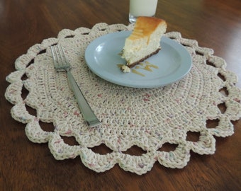 May include: A white crocheted placemat with a scalloped edge and a light blue plate with a slice of cheesecake on it. A silver fork is on the placemat.