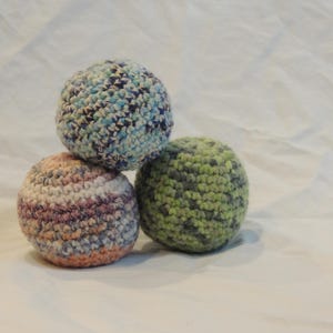 Puede incluir: Tres bolas de crochet en diferentes colores y patrones. La bola de arriba es azul y blanca, la bola del medio es rosa y blanca, y la bola de abajo es verde.