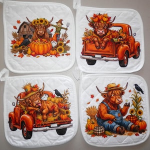 May include: A set of four white quilted pot holders featuring colorful autumn-themed illustrations of Highland cows. The designs include cows with pumpkins, sunflowers, a rustic barn, a scarecrow, and an orange pickup truck with fall foliage.