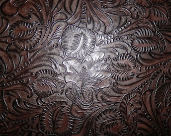 May include: Close-up of a brown leather surface with an embossed floral pattern. The design features detailed leaves and flowers, creating a textured, decorative effect. The leather has a glossy finish.