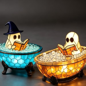 May include: Two stained glass lamps shaped like bathtubs with ghosts inside. The left lamp is blue with a ghost wearing a dark blue hat reading a book. The right lamp is amber with a ghost wearing round glasses reading a book with a small cup.