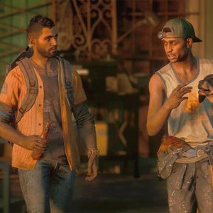 Puede incluir: Dos personas de pie juntas, una con camisa naranja sobre una camiseta gris con vaqueros y mochila, la otra con camiseta blanca sin mangas y pantalones oscuros, sosteniendo un perro pequeño negro y fuego con un dispositivo de apoyo con ruedas.