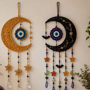 Può includere: Due decorazioni da parete a forma di mezzaluna con texture all'uncinetto, motivi centrali a occhio di Allah e fili di perline pendenti con dettagli a stella e cristallo. Una luna è giallo senape, l'altra è nera con decorazioni a pipistrello.