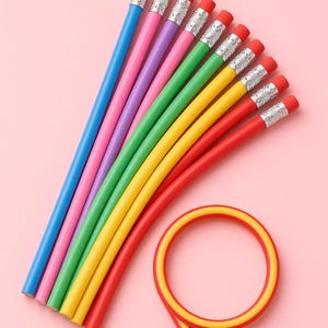 Puede incluir: Un conjunto de lápices flexibles en azul, rosa, morado, verde, amarillo y rojo, cada uno con una virola de metal plateado y una goma de borrar rosa. Un lápiz rojo y amarillo está enrollado en forma circular, mientras los otros están en abanico.