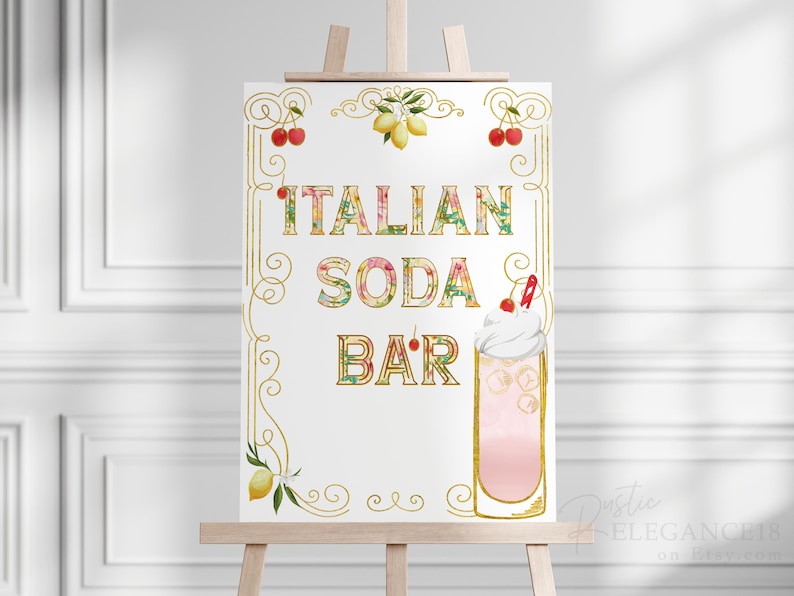 Puede incluir: Un cartel blanco con letras doradas y detalles florales que dice "Italian Soda Bar". El cartel est&aacute; en un caballete y presenta una soda italiana rosa y blanca con una cereza en la parte superior.
