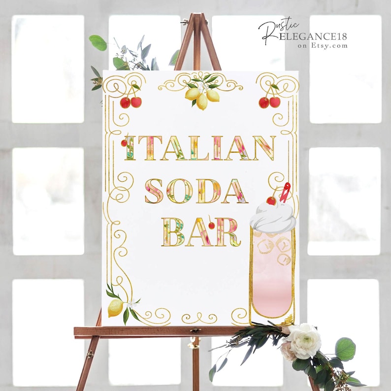 May include: A white sign with gold lettering that reads "Italian Soda Bar". The sign is decorated with lemons, cherries, and a floral design. A glass of pink soda with whipped cream and a cherry on top is pictured on the sign.