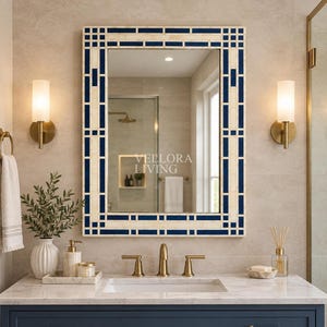 May include: A rectangular wall mirror featuring a geometric frame with alternating cream-colored and deep navy blue rectangular inlays. The glass surface displays the text VELLORA LIVING in white lettering, reflecting a bathroom interior.