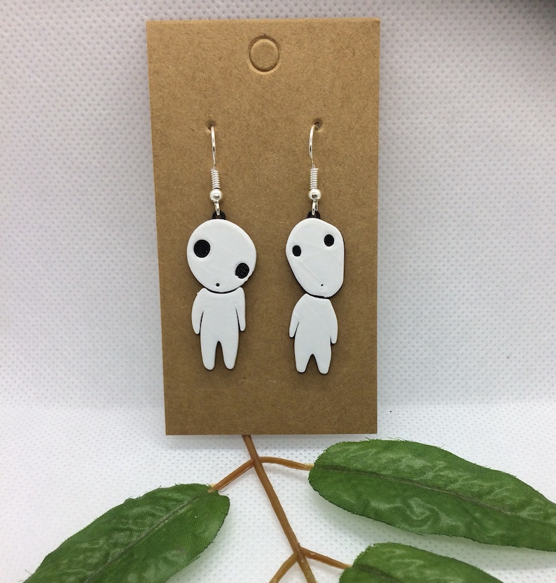 May include: White dangle earrings with a small white figure with black eyes on each earring.