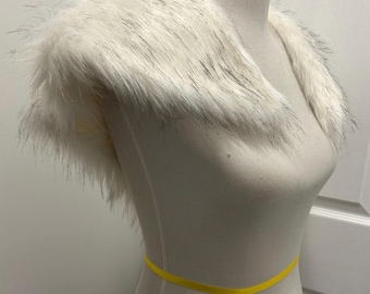 May include: A faux fur collar in white with gray accents, displayed on a mannequin. The collar is designed to be worn around the shoulders and neck. A yellow ribbon is wrapped around the mannequin's waist.