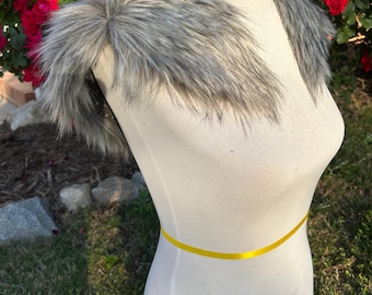 May include: A gray faux fur collar displayed on a white mannequin. The collar is fluffy and has a layered texture. A yellow ribbon is wrapped around the mannequin's waist. Red roses are in the background.